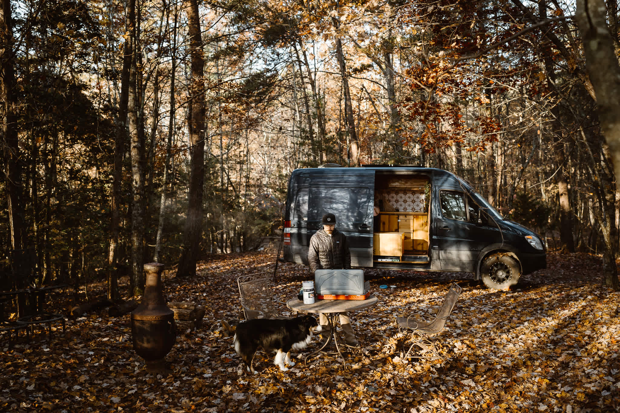 Secluded campsite in the woods featuring a table and chairs set up, firepit & chiminea. Great location for our Sprinter 144 Campervan