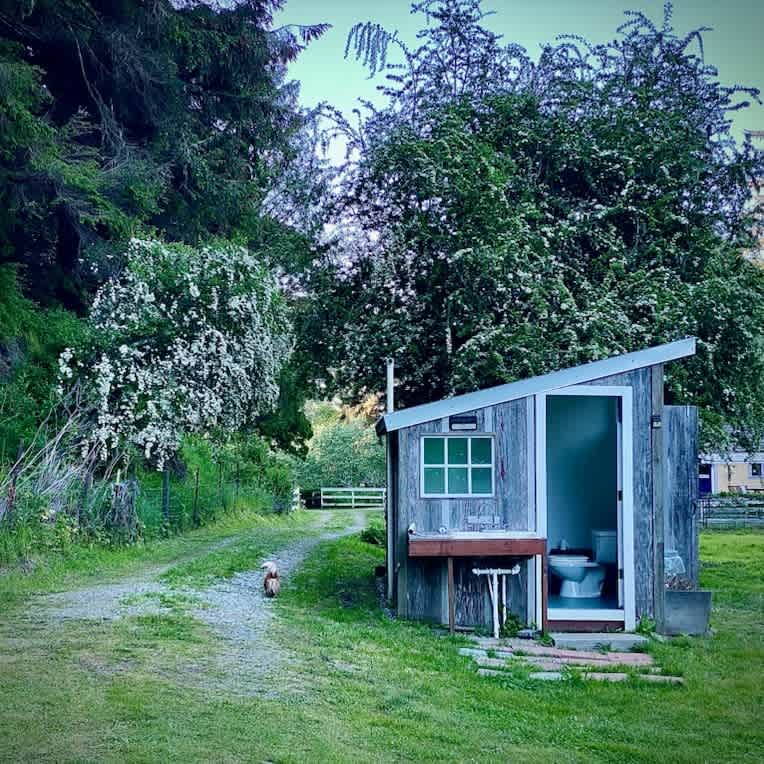 A converted chicken coop has a half-bath (in photo) in front, and a second bathrom with double shower, accessible from a barn doow on the side. (Slightly open in photo)