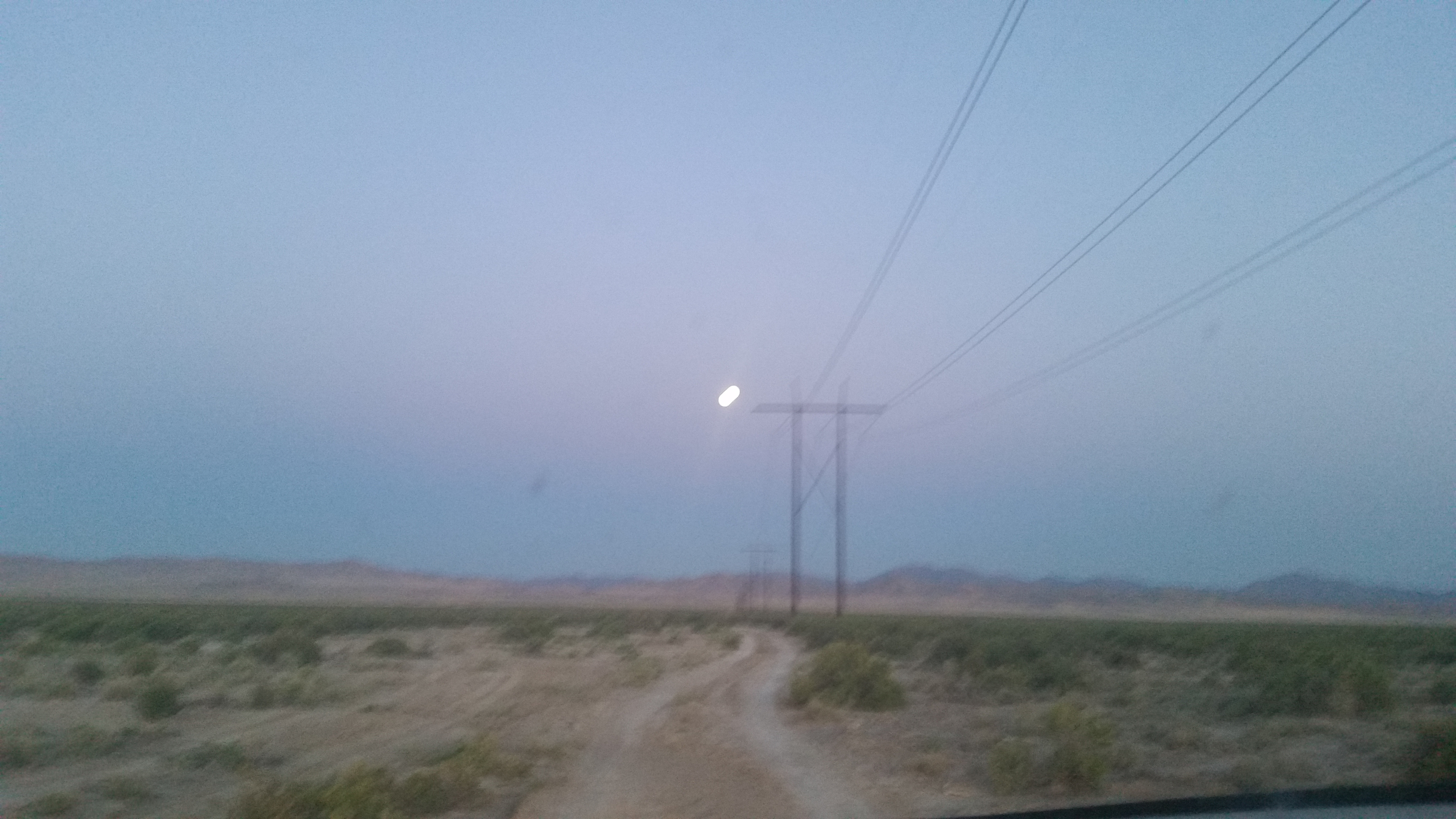 Giant full moon coming up over the power poles on the road in...