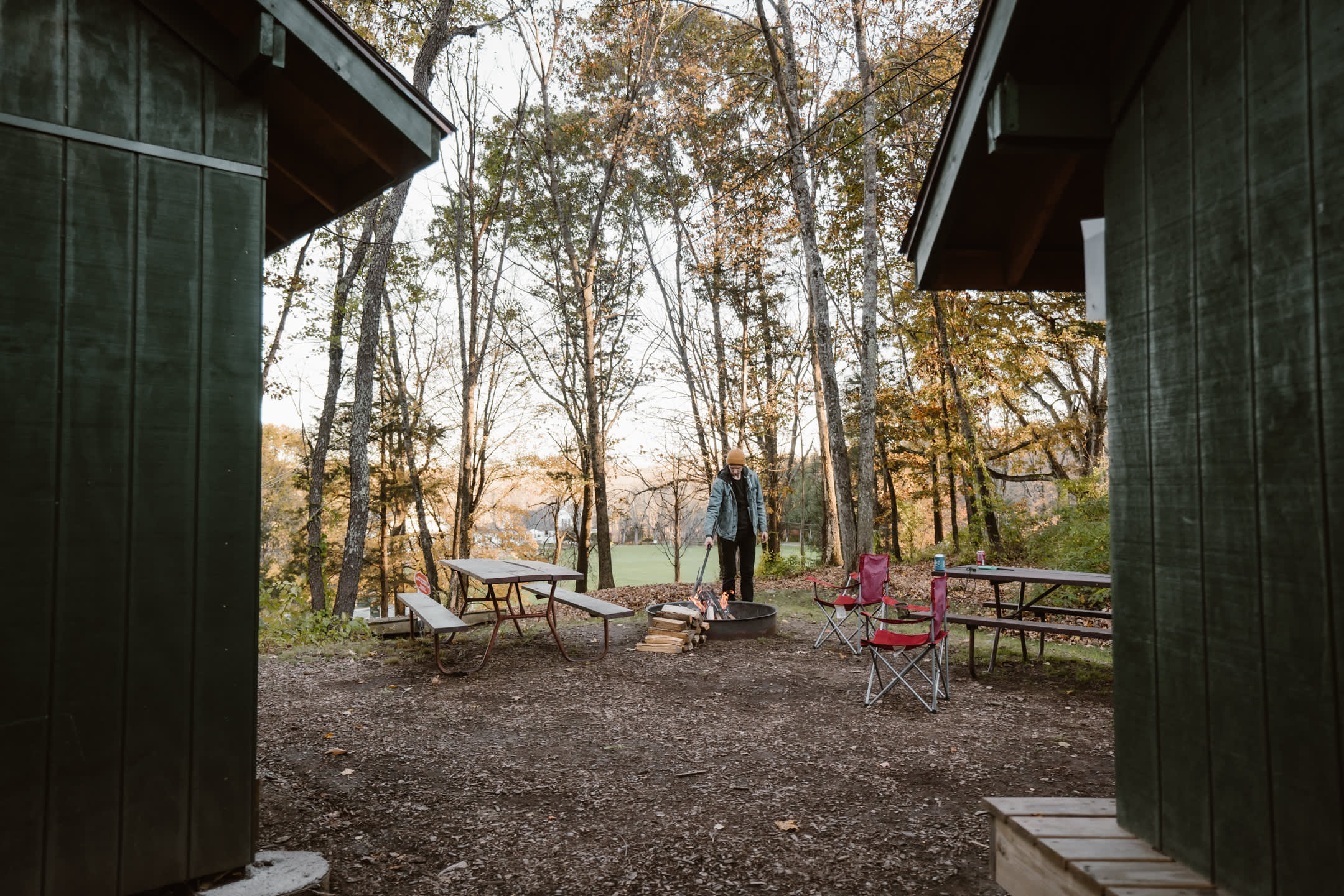 Two shelters side by side with a campfire ring and two picnic tables.