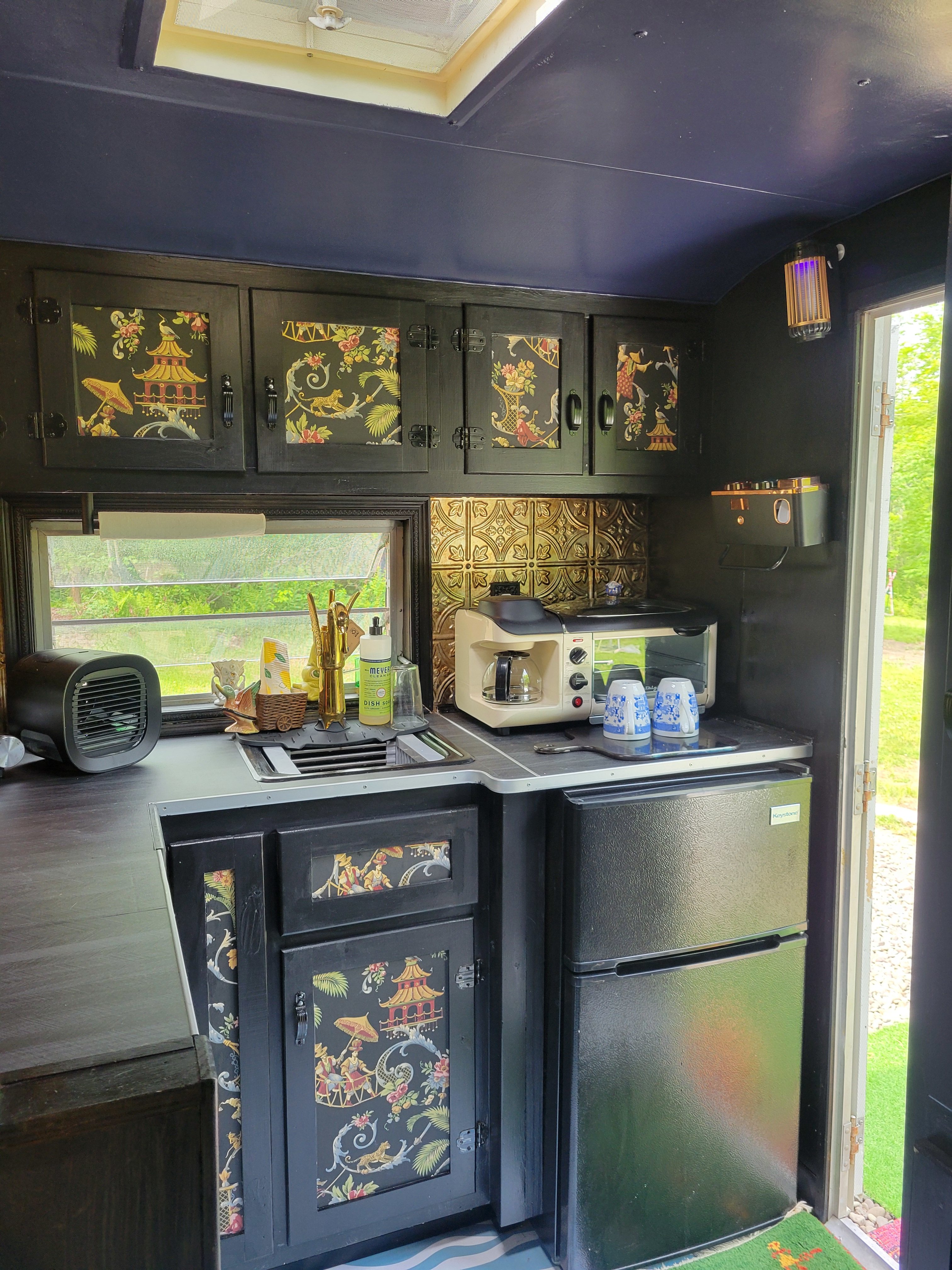 Smaller camper kitchenette, electric hot plate, all-in-one toaster, coffeemaker griddle, and mini fridge. The sink has hot and cold filtered water. 