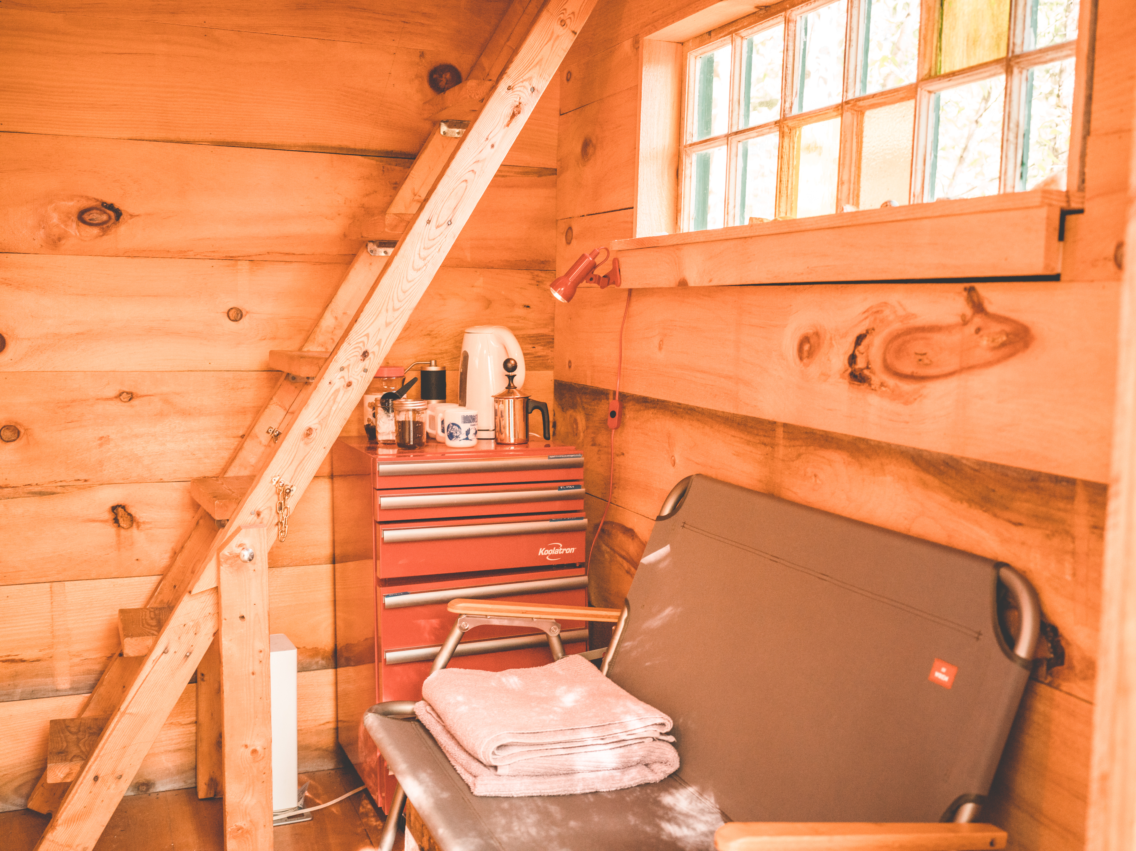 downstairs of the cabin with bench, towels, heater, fridge, and kitchenette. small fridge with cups, mugs, plates, napkins, silverware, french press, water boiler, and coffee grinder. water is potable and can be taken from the outdoor sink area. the stairs lead up to the bed area.