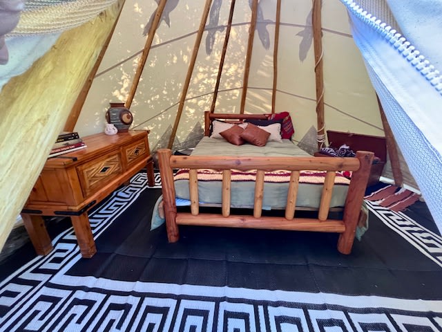 Cozy tipi interior with comfortable queen size bed and all of the linens/blankets