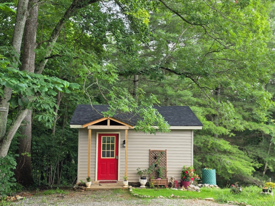 The cottage is nestled under a canopy of trees and surrounded on three sides by wooded slopes.