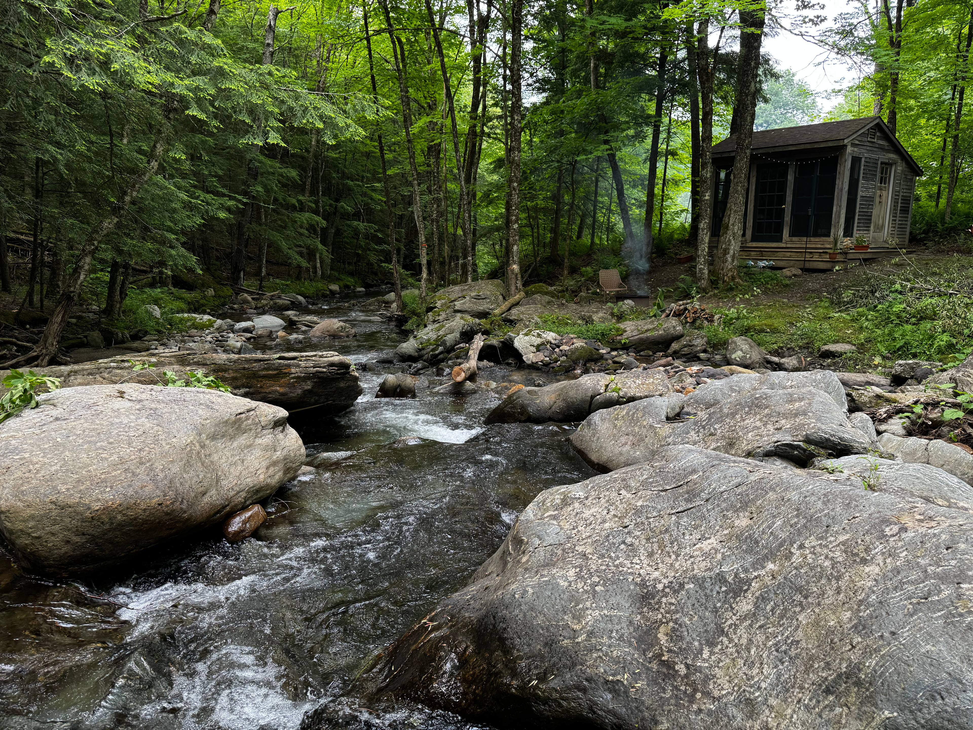 Cabin from the Brook’s Perspective
Here’s the cabin as seen from the brook’s point of view—tucked into trees, surrounded by ferns, just out of reach from the rush of everyday life. Imagine ending your day here: a fire crackling in the fire pit, the gentle sound of water as nature’s white noise.

You’re working on unplugging, reflecting, and being present. Your hand habitually reaches for your phone, but the loading wheel reminds you it won’t cooperate here. So you put it down. You look around. And a little piece of your soul starts to unwind....

Welcome. I hope you enjoy your stay.