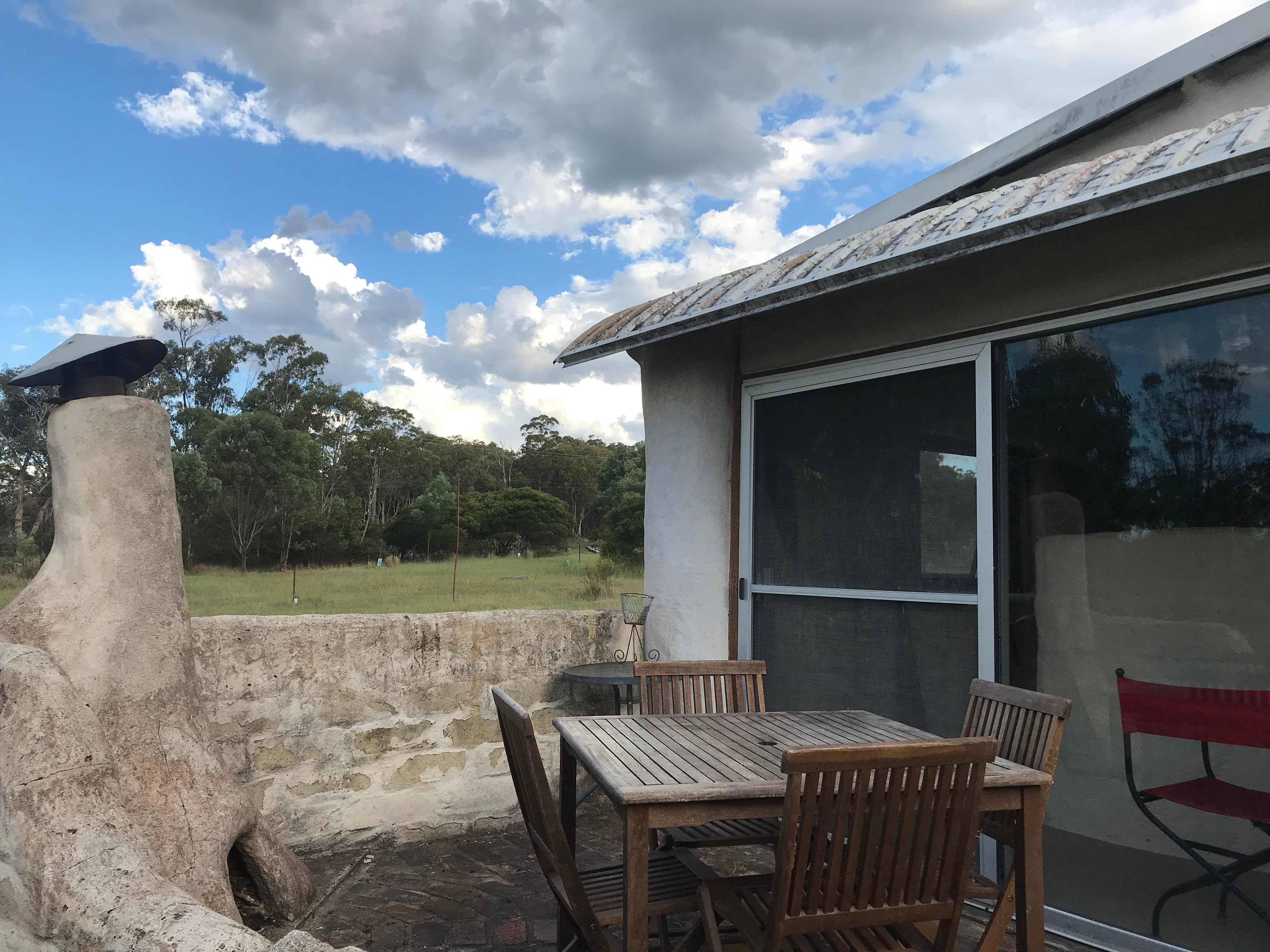 Outdoor patio, picnic table, fireplace and sliding door to the straw bale bedroom. This room was originally built as sleeping accommodation for WWOOFERs (Willing Workers On Organic Farms). In the current configuration, the room has two single beds and two sofa chairs. The room is designed with passive thermal heating through sunshine warming the mud-brick dividing wall during the day. 

PLEASE NOTE: the toilet/laundry is 20m walk in a second separate building and the kitchen/shower is 60m walk in a third separate building. 