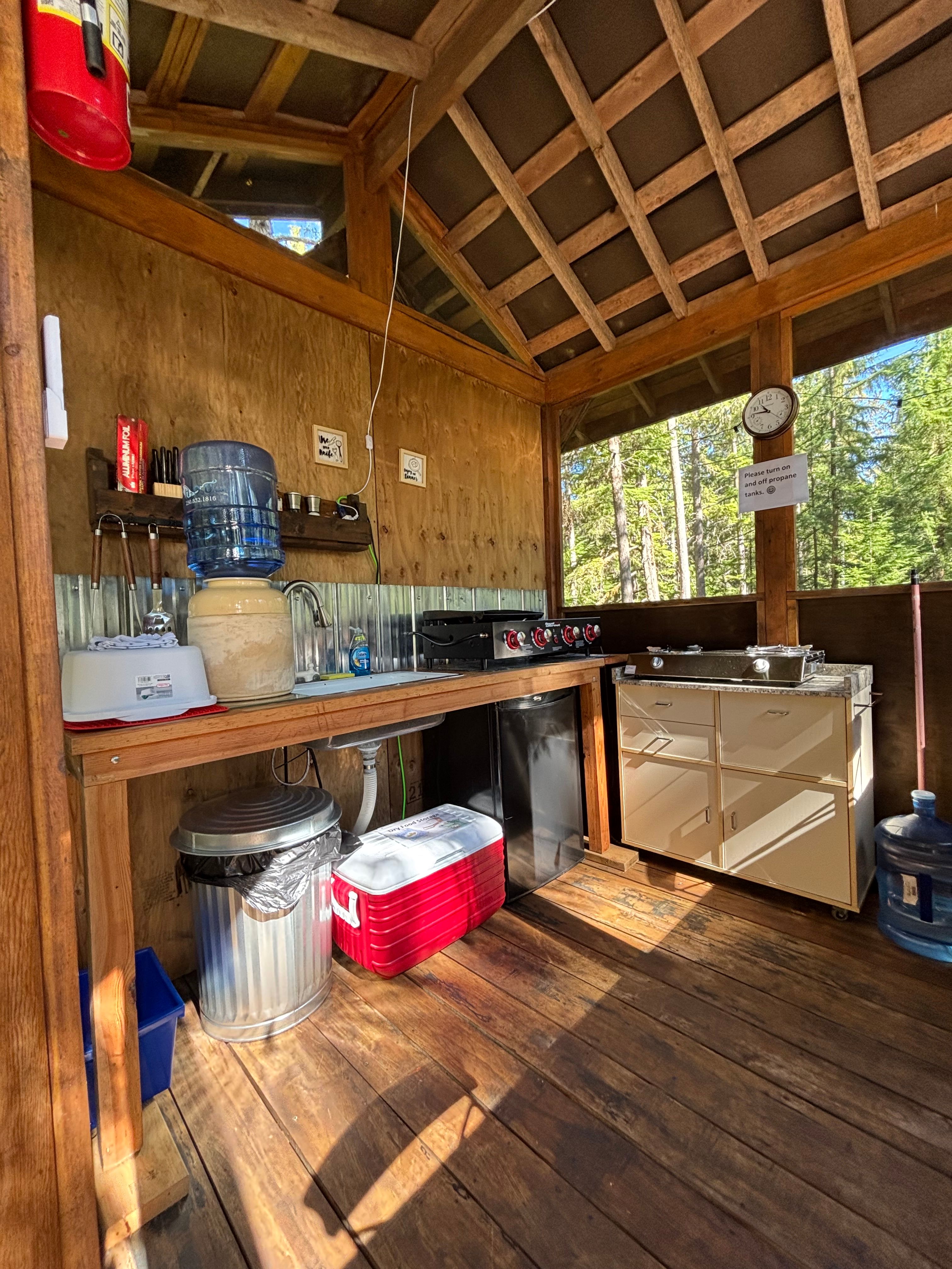 Inside the open air kitchen shack.  There is a mini fridge, cooler to store dry goods, seating and eating bar , a propane 2 burner cooktop and a grill and flat top cooking station.
Fully stocked with pots, pans, dishes, cutlery and cooking utensils.