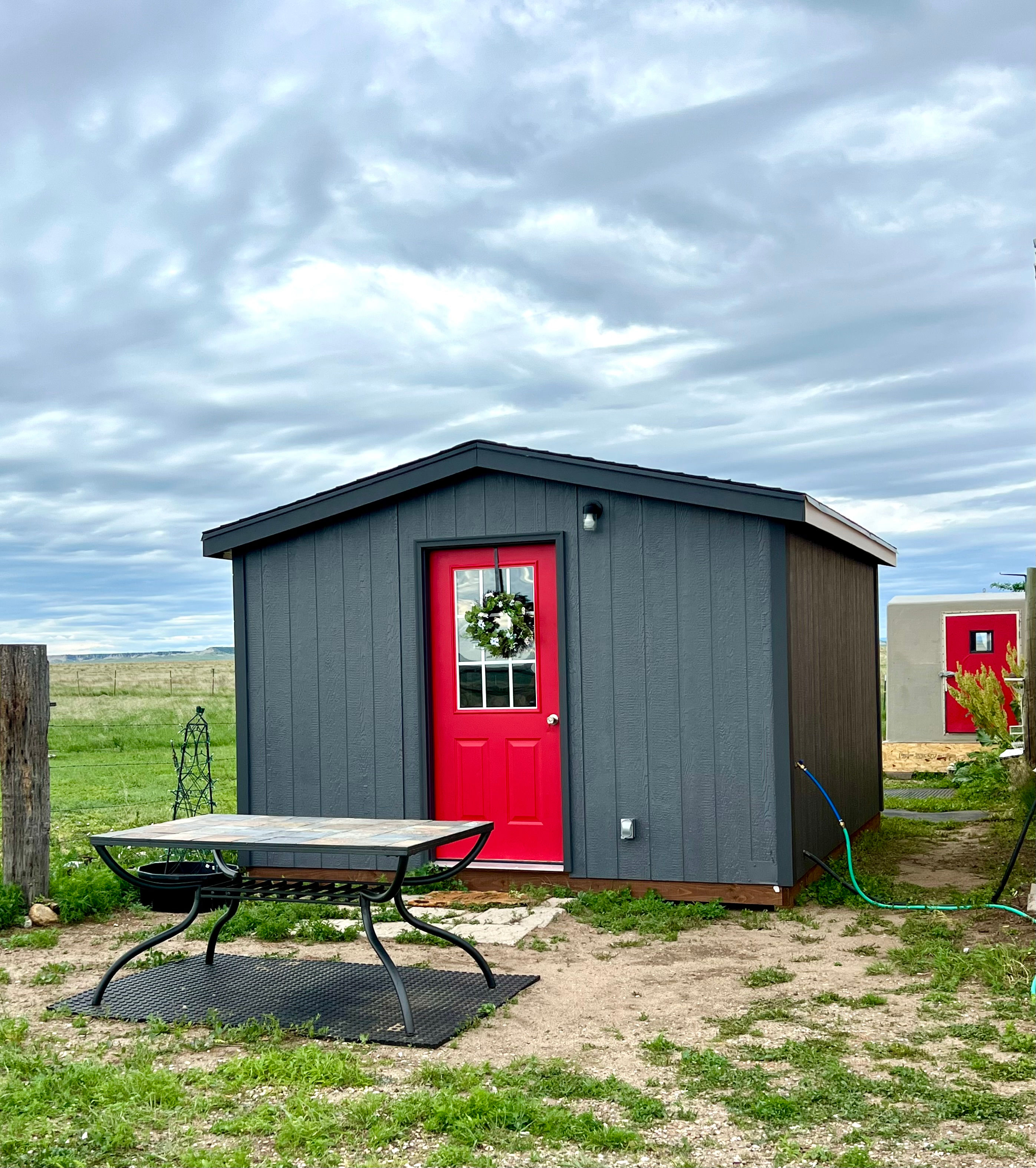 BADLANDS BUNKHOUSE Prairie Retreat, a cozy 12’ x 14’ insulated cabin with a tiny kitchen, stovetop, fridge, sink, basic kitchen supplies, TV, AC and heat. The BADLANDS BATHHOUSE in the background is also part of your private site, and has a compost toilet and hot/cold shower.