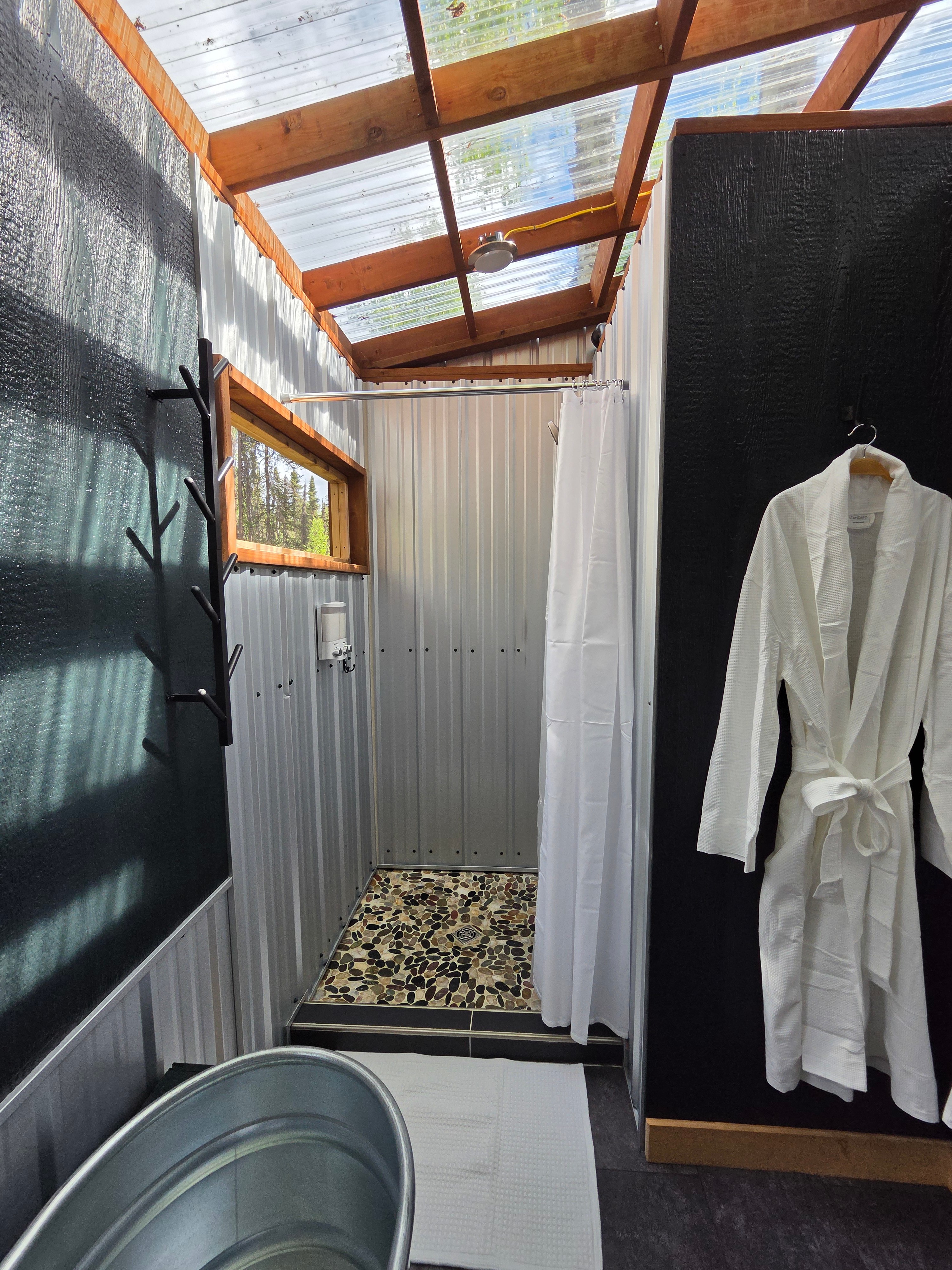A secluded, nature-inspired shower with a clear roof, offering sweeping views of the tree canopy and sky.