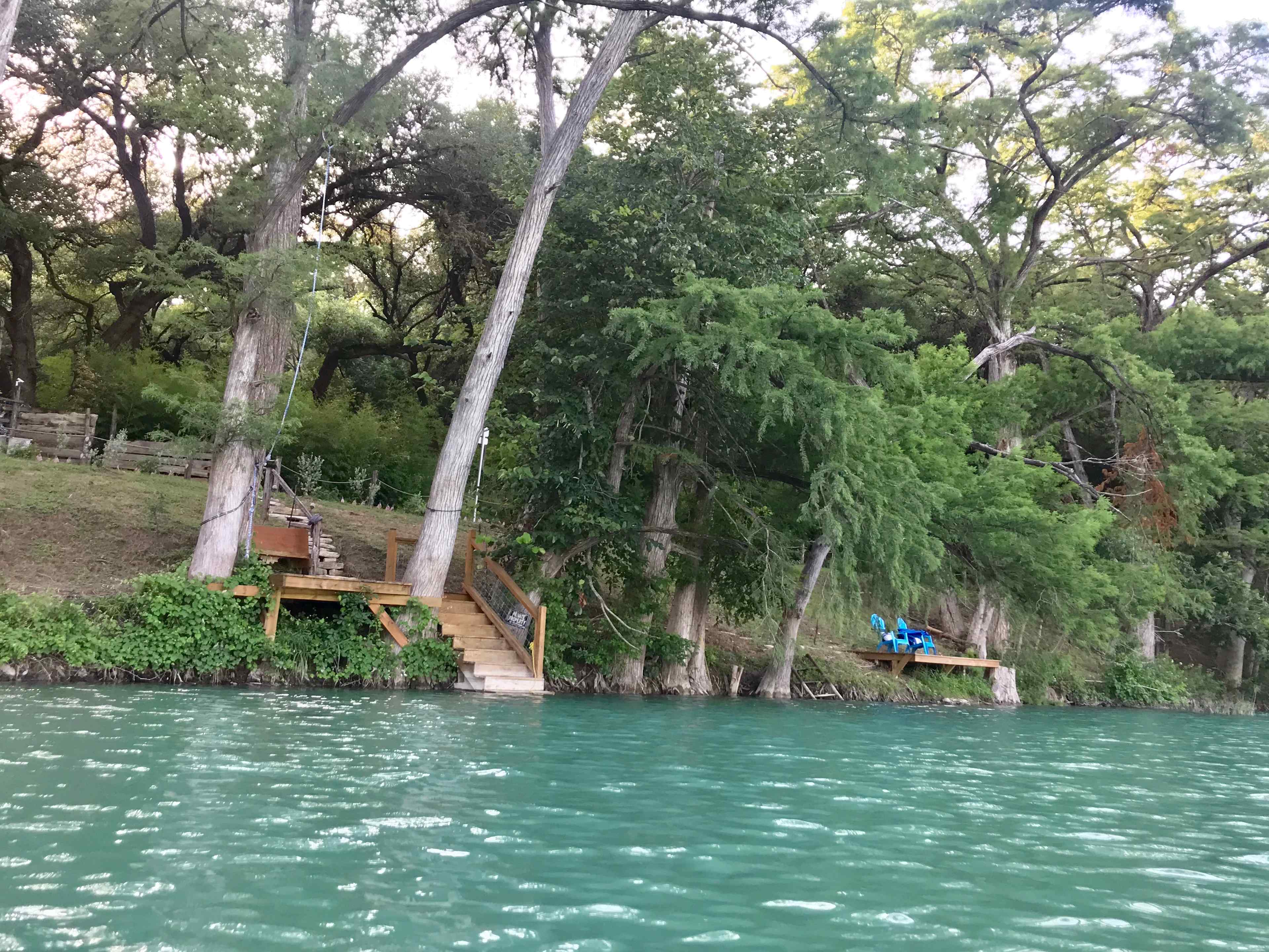 a water view showing both docks. the one on the left has rope swings, and steps for entering and exiting the river with floats, kayaks, SUPS, etc. The one on the right, is better suited for fishing, relaxing, meditating. There is a steel ladder adjacent to it.