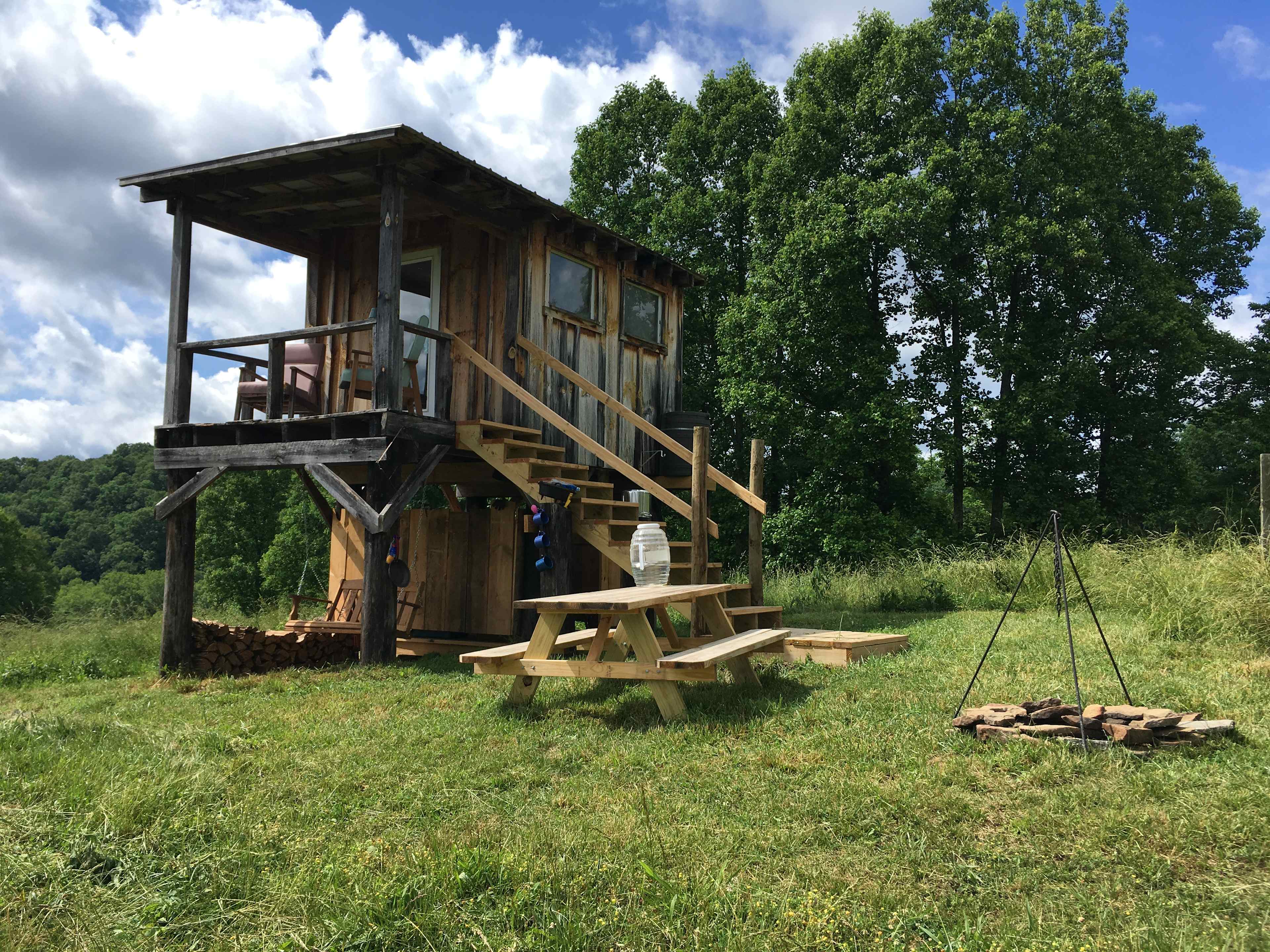 The Reformed Hunting Cabin features a firepit with hanging cookpot, cookware in the cabin, compostable toilet, and swing. 