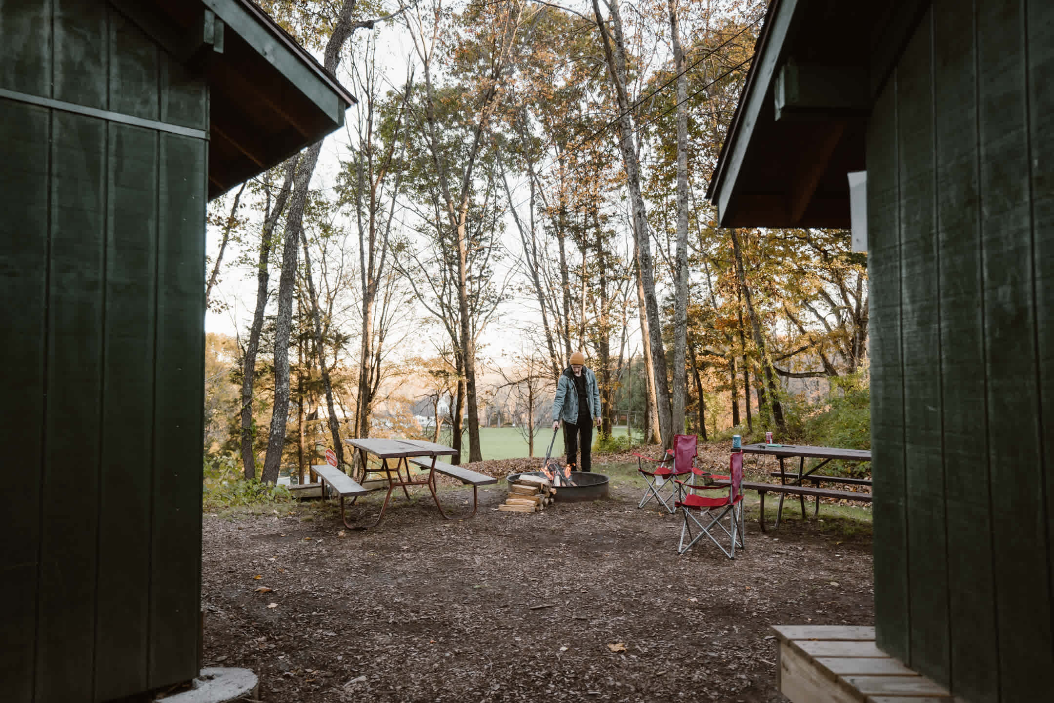 Two shelters side by side with a campfire ring and two picnic tables.